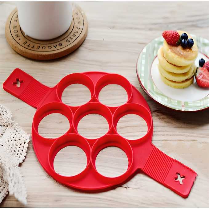 Top view of red silicone non-stick pancake mold with seven round slots on a griddle